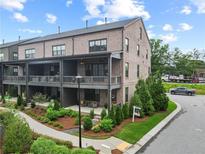 Beautiful brick townhouse with a covered porch, landscaped yard, and a sidewalk on a sunny day at 6460 Cortland Walk, Alpharetta, GA 30005