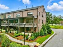 Charming brick townhome featuring a landscaped yard and inviting covered porches for outdoor enjoyment at 6460 Cortland Walk, Alpharetta, GA 30005