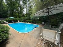 Relaxing pool area with chairs, table and umbrella, surrounded by mature trees and greenery at 2671 Club Forest Se Ct, Conyers, GA 30013