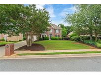 Brick two-story home with a well-manicured lawn and mature trees, enhancing curb appeal at 6695 Buckingham Cir, Cumming, GA 30040