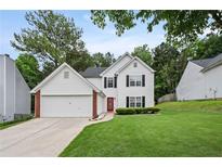 Charming two-story home featuring a well-manicured lawn, attached garage, and a vibrant red front door at 1047 Woodsong Pass Ct, Lawrenceville, GA 30043