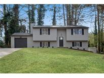 Charming two-story home with gray siding, a well-manicured lawn, and a paved driveway leading to an attached garage at 3414 Dearwood Sw Dr, Lilburn, GA 30047