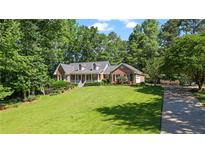 Charming brick home with manicured lawn, mature trees, and inviting front porch at 7376 Bates Dr, Cumming, GA 30040