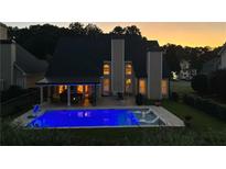Backyard view of the house with an illuminated blue inground pool and covered patio at dusk at 5440 Old Haven Ct, Cumming, GA 30041