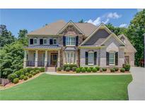 Beautiful two-story home featuring a stone and brick facade, manicured lawn, and covered front porch at 255 Beech Tree Holw, Sugar Hill, GA 30518