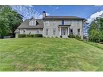 Stately grey brick home featuring a manicured lawn, classic architectural details, and lush landscaping at 1168 Atcheson Ln, Atlanta, GA 30338