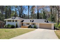Charming white brick home featuring a long driveway, attached garage and manicured front yard and wooded backdrop at 1978 Fisher Ne Trl, Atlanta, GA 30345