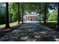 Long driveway leading to a brick home with white columns and a large front lawn, partially shaded by mature trees at 4790 Shallowford Rd, Roswell, GA 30075