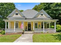 Charming yellow two-story home with inviting front porch, lush landscaping, and American flag at 161 N Barton St, Norcross, GA 30071