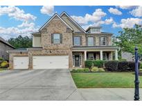 Charming brick home featuring a three-car garage, manicured lawn, and welcoming front porch at 4191 Secret Shoals Way, Buford, GA 30518