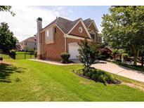 Well-manicured lawn and two-story brick home featuring an attached two-car garage and mature trees at 2484 Mossy Branch Dr, Snellville, GA 30078