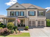Charming two-story home with white brick, shuttered windows, two-car garage, and professionally landscaped front yard at 4440 Atwood Dr, Cumming, GA 30040