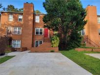 Brick townhome showcasing a red front door and staircase access with a concrete driveway and mature trees at 115 Davis Mill Ct, Lawrenceville, GA 30044
