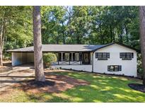 Charming single-story home with white brick, black trim, manicured lawn, and attached carport in a wooded setting at 1582 Pine Cir, Austell, GA 30168