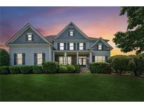 Stately two-story home boasts a lush front lawn, manicured hedges, and classic architectural details against a vibrant sunset backdrop at 2581 Trailing Ivy Way, Buford, GA 30519