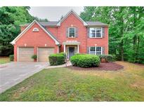 Charming two-story red brick home featuring a well-manicured lawn, attached two-car garage, and lush landscaping at 5765 Woodstone Dr, Cumming, GA 30028