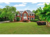 Charming two-story red brick home with a lush green lawn, complemented by mature trees and manicured landscaping at 209 Breckenridge Ct, Canton, GA 30115