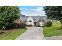 Charming brick home featuring a well-maintained lawn, mature trees, and a paved driveway leading to the garage at 3834 Hawk Tail Dr, Loganville, GA 30052