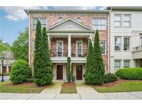 Beautiful brick townhome featuring second story balconies, symmetrical evergreens, and manicured landscaping at 1858 Preserve Way, Atlanta, GA 30341