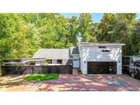 Contemporary home featuring a two-car garage, black privacy fence, brick driveway and mature landscaping at 1048 Indian Hills Pkwy, Marietta, GA 30068