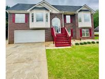 Traditional brick home features a two-car garage, manicured lawn, and red accents around the windows and front steps at 80 Fields Creek Way, Covington, GA 30016