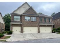 Townhome exterior with a three-car garage, brick facade, and covered entrance on a cloudy day at 805 Pleasant Hill Nw Rd # 53, Lilburn, GA 30047