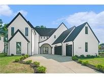 Stunning exterior of a modern home with black trim, arched doorway, and a concrete driveway leading to a two-car garage at 115 Thome Dr, Alpharetta, GA 30022