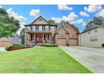 Beautiful brick home featuring manicured lawn, two car garage, covered porch and a bright red front door at 2612 Back Creek Chase, Dacula, GA 30019