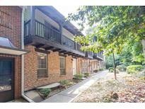 Brick townhome showcasing a second-story balcony, complemented by lush greenery and manicured landscaping at 7307 Cardigan Cir, Sandy Springs, GA 30328