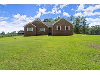 A charming brick home has a large lawn, mature trees and a barn in the background at 3950 Chattahoochee Rd, Cumming, GA 30041