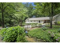 Inviting home exterior featuring stone facade, mature landscaping, and charming wooden bridge at 7265 Hunters Branch Dr, Sandy Springs, GA 30328