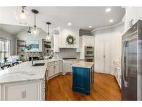 Bright kitchen boasts white cabinets, a blue island, stainless appliances, granite counters and hardwood floors at 5173 Brendlynn Dr, Suwanee, GA 30024
