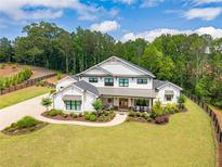 Stunning modern farmhouse with lush landscaping, a sprawling lawn, and a charming covered front porch at 6301 New Bethany Rd, Buford, GA 30518