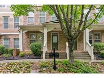 Inviting brick townhouse with a covered porch, complemented by lush landscaping and a charming tree at 4358 Grove Field Ct, Suwanee, GA 30024