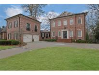 Elegant brick home featuring a circular driveway, manicured lawn, and a detached two-car garage at 4084 Peachtree Dunwoody Rd, Atlanta, GA 30342