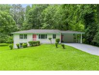 Charming single-story home with a lush green lawn, pink door, and carport, nestled among mature trees at 2343 Dawn Dr, Decatur, GA 30032