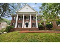Stately brick home featuring white columns, black shutters, and a manicured front lawn on a lush, green lot at 1595 Bakers Glen Dr, Atlanta, GA 30350
