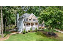 Charming brick and siding home featuring a covered porch, well-manicured lawn, and mature trees at 5301 Regency Lake Ct, Sugar Hill, GA 30518
