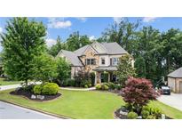 Charming brick home featuring manicured lawn, stone accents, and mature trees on a sunny day at 1980 Marcia Overlook Dr, Cumming, GA 30041