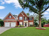 Charming two-story red brick home with manicured lawn, black shutters, two car garage, and mature shade tree at 608 Chickory Ct, Woodstock, GA 30188