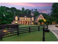 A brick two-story home has a manicured front yard with a black fence, plus a long driveway at dusk at 325 Edwards Brook Ln, Canton, GA 30115