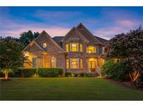 Beautiful brick home featuring manicured lawn, mature landscaping and charming architectural details at dusk at 979 Pathview Ct, Dacula, GA 30019
