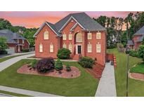 Charming two-story brick home boasts a lush lawn, mature trees, and inviting curb appeal at 240 Flowers Cove Ln, Lilburn, GA 30047