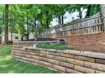 Landscaped backyard features a retaining wall with lush greenery and mature trees at 2633 Hanriva Ct, Dacula, GA 30019