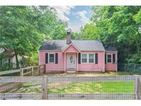 Charming pink cottage-style home with black shutters and a well-maintained front yard surrounded by mature trees at 207 Walthall Nw St, Marietta, GA 30064