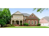 Elegant brick home featuring a covered porch with columns, a balcony, manicured lawn, and lush landscaping at 1565 Briergate Dr, Duluth, GA 30097