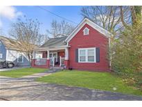 Charming red home featuring a cozy front porch, complemented by green grass and mature trees at 1081 Longley Nw Ave, Atlanta, GA 30318