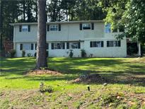 Two-story home with light siding, black shutters and a green lawn surrounded by tall trees at 2510 Lakeshore Ne Dr, Conyers, GA 30012