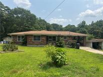 Quaint brick home featuring large front yard, small shrubs, and a covered carport with a small building nearby at 547 Morningside Dr, Lawrenceville, GA 30043