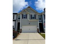 Charming townhome featuring a two-car garage and neat landscaping under a partly cloudy sky at 776 Woodstock Grove Dr, Woodstock, GA 30188